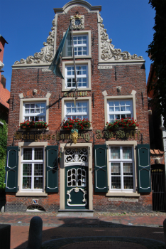 Fassade der historischen Weingro&szlig;handlung J.W. Wolff, erbaut 1800, mit reich verziertem Backsteingiebel, gr&uuml;nen Fensterl&auml;den, goldener Schrift und detailreicher Eingangst&uuml;r mit dekorativen Ornamenten.