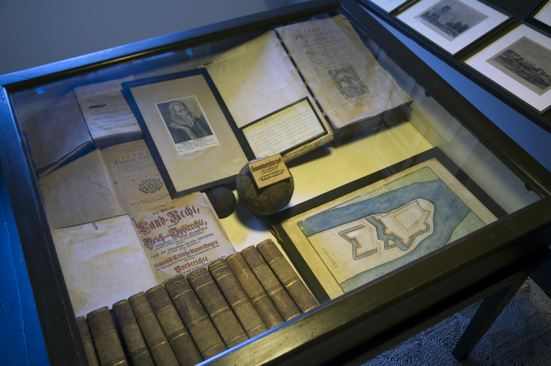 Museum: Vitrine mit historischen Dokumenten und B&uuml;chern. Ausgestellt sind Landkarten, Schriftst&uuml;cke, ein Portr&auml;t und weitere Exponate.